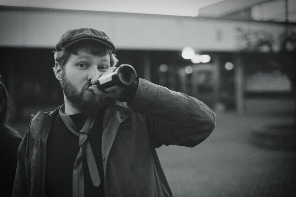 Daniel Sand mit Schiebermütze trinkt aus einer Flasche, Schwarzweißfoto